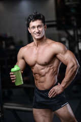 Fototapeta premium Handsome fitness model holding a shaker in the gym gain muscle.