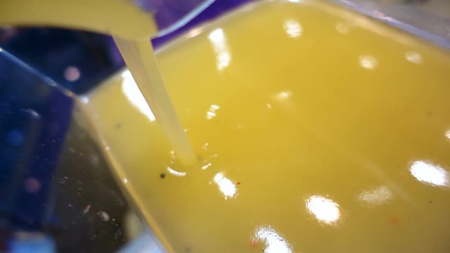 Orange thick gel is poured into a glass container, and reflects light. Slow mo, slow motion, slo mo, high speed camera, 240fps, 250fps