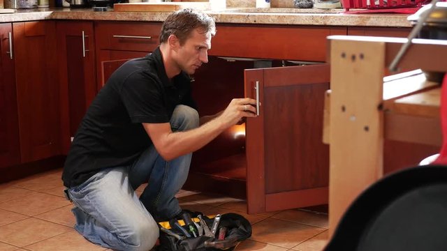 Handyman fixing cabinet with screwdriver in kitchen