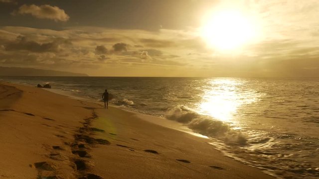 Surfer holding surfboard and walking on the beach during sunset