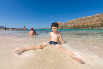 Balos beach. The west coast of the peninsula Gramvousa. Joyful boy sitting in water on the beach. Crete. Greece. Distortions. Wide-angle lens.