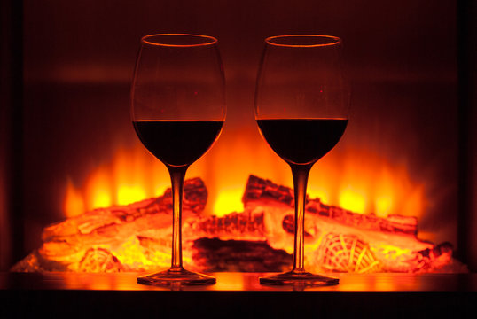 Two glasses of wine next to the fireplace.