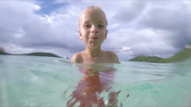slow motion video of child spitting water at camera on tropical beach