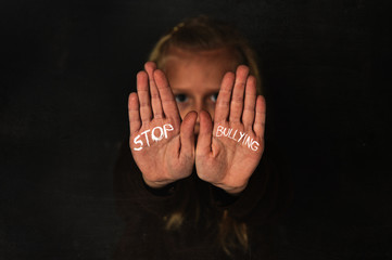 cute schoolgirl scared sad asking for help showing hands with stop bullying text written on her palm