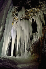 Winter icicles iluminated with battery and candles. Frozen cave in Slovakia. Stalactite and stalagmite. Exploration depths of the earth.
