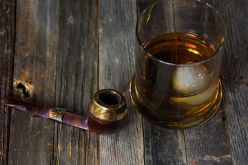 whiskey drink in glass with ice ball and vintage smoking pipe on rustic wood