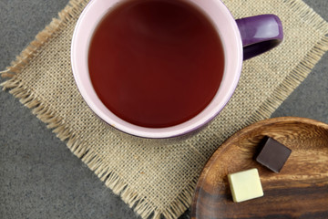 Cup of tea and two pieces of chocolate on a wooden plate.