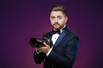 successful professional photographer in tuxedo use DSLR digital camera on dark background