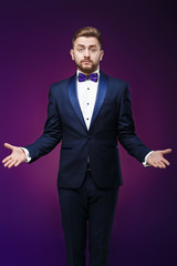 Handsome man in tuxedo and bow tie is surprised, throws his hands. compere in fashionable, festive clothing