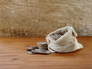 Burlap bag with coins on a rustic wood background