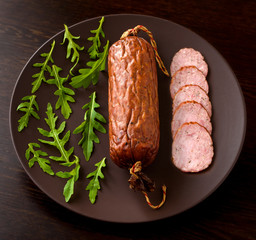 Smoked sausage with arugula lettuce on a dark brown background