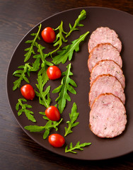 Smoked sausage with arugula lettuce and tomatoes on a dark brown background