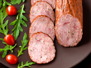 Smoked sausage with arugula lettuce and tomatoes on a dark brown background