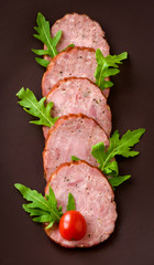 Smoked sausage with arugula lettuce and tomatoes on a dark brown background