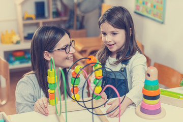 Woman looking at kid playing with didactic colorful toys indoors - preschool