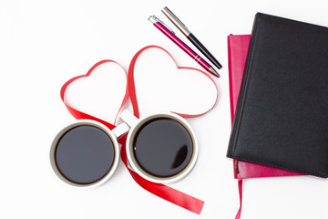 coffee, hearts from red ribbon, pink and black diaries with pens on a white background.