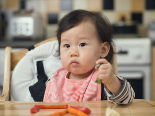 Asian baby girl eating roasted vegetable at home kitchen