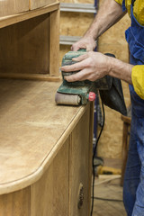 Carpenter restores vintage the wooden a sideboard by an electric of the grinding machine.