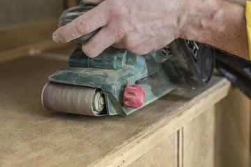 Carpenter restores vintage the wooden a sideboard by an electric of the grinding machine.