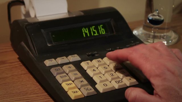 Hand operates old retro calculator at workstation