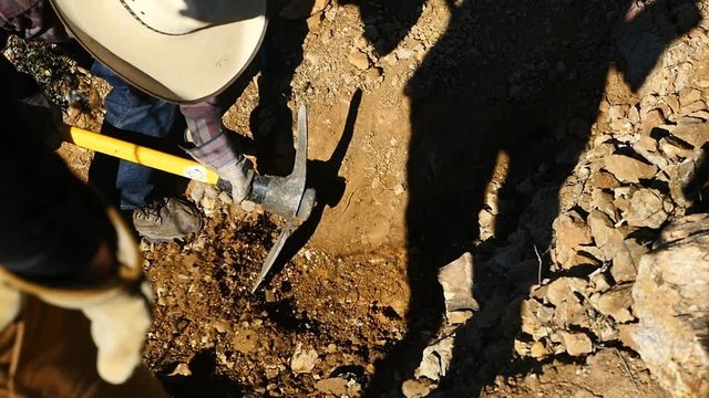 A man digging in the desert with a pickaxe