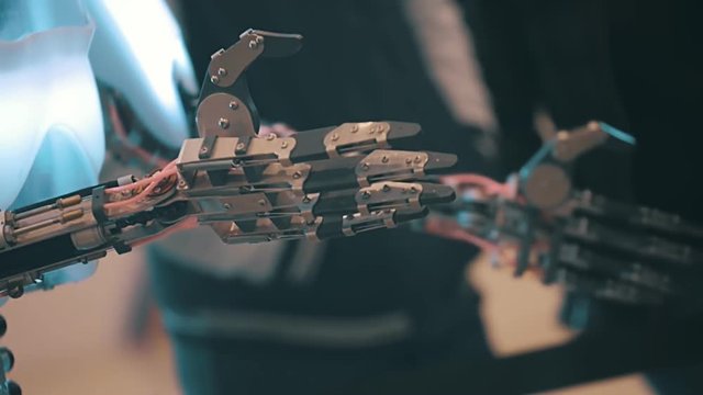 Humanoid robot from metal lowers his arm and moves fingers