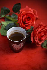Obraz na płótnie Canvas Valentine's Day: Cup of coffee or warm beverage and red roses on dark red background