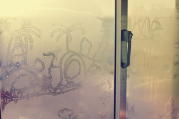 Childhood drawing on a cold fogged window background