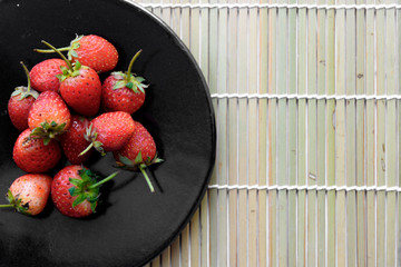 The pile of fresh strawberry on the black dish,Wooden tray backg