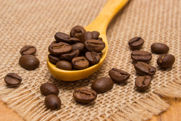Heap of coffee beans with wooden spoon on jute canvas