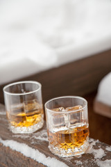 Two whiskey glasses in the snow on a winter background.