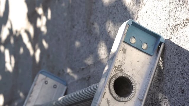 Close up shot of the end of a ladder being placed against a cinder-block wall before someone climbs it.