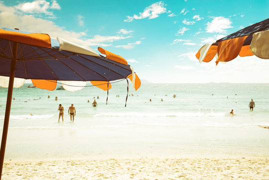 An Umbrella At Tropical Beach With Blurred People Relaxing On Beach In Summer. Vintage Color Tone