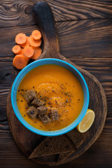 Bowl of carrot soup on a rustic wooden background, above view