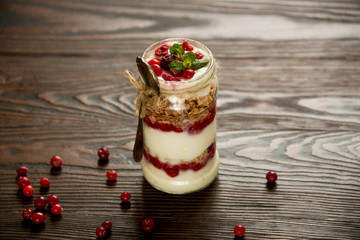 Healthy breakfast - layered dessert with yogurt, granola, jam, raspberries, cranberries and mint on wooden background