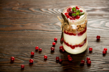 Healthy breakfast - layered dessert with yogurt, granola, jam, raspberries, cranberries and mint on wooden background