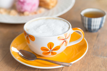 A Cup of cappuccino coffee in a white cup with saucer on the wooden table.