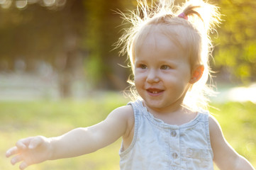 Cheerful little girl in a summer park at sunset