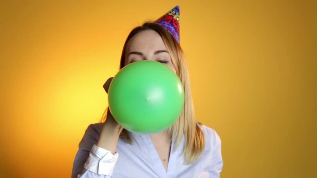 Girl inflating a balloon on a yellow background