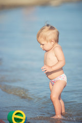 Baby playing on the sandy beach and in sea water. Cute little kid with toys on sand tropical beach. Ocean coast.