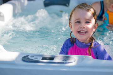 Cute girl caucasian toddler blonde hair blue eyes bright rash vest playing in water full of joy and happiness learning to swim and splashing about in the sun in the jacuzzi 