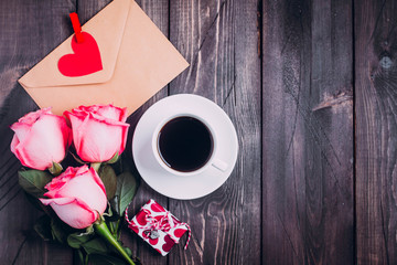 Valentines day background. Cup of coffe, pink roses, gift and envelope with paper heart. Topview with copy space
