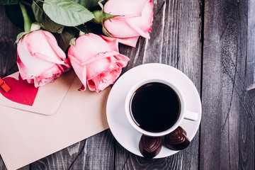 Valentines day background. Cup of coffee with chocolate candies and pink roses, envelope with paper heart. Top view with copy spaces