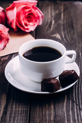 Valentines day background. Cup of coffee with chocolate candies and pink roses, envelope with paper heart. Top view with copy spaces