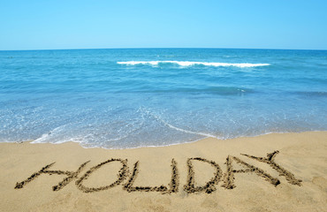 Holiday written on sandy beach, in the background sea and blue sky.