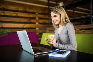 Young girl with cup in hands look at laptop  at working place