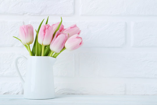 Bouquet of tulips in jug on brick wall background