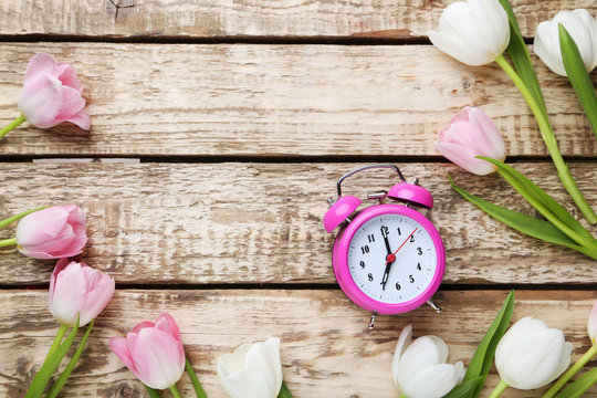 Bouquet of tulips with alarm clock on grey wooden table