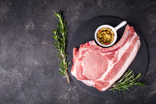 Raw meat on dark background. Raw pork steak with herbs, oil and spices. Cooking meat. Copy space. Top view