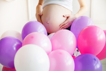 pregnant woman with a big belly is behind the colored balloons
